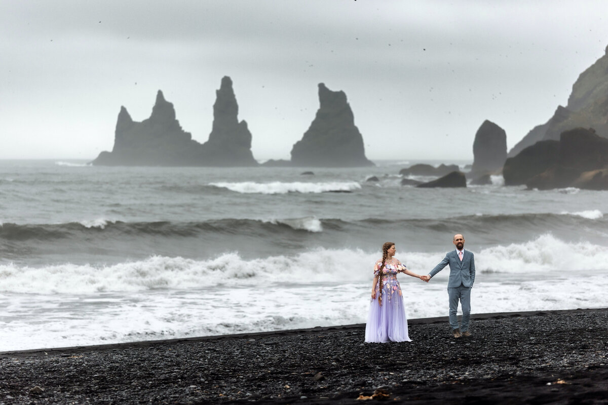 A couple explores the mystical landscapes of Iceland's lava fields, their hands clasped tightly as they navigate their journey together