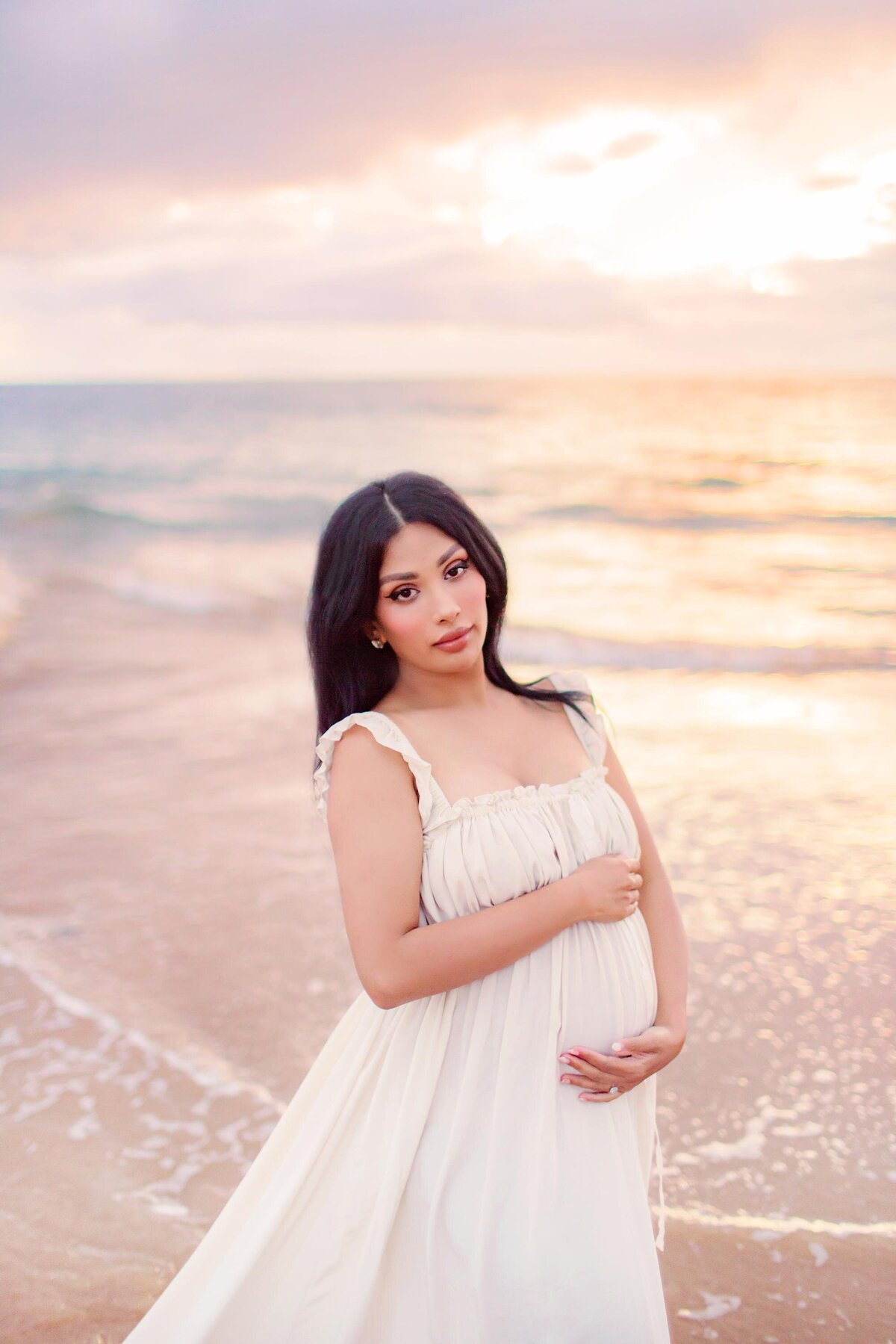 Beautiful pregnant woman in ruffled maternity dress looks at the camera and poses for her babymoon pics on Maui