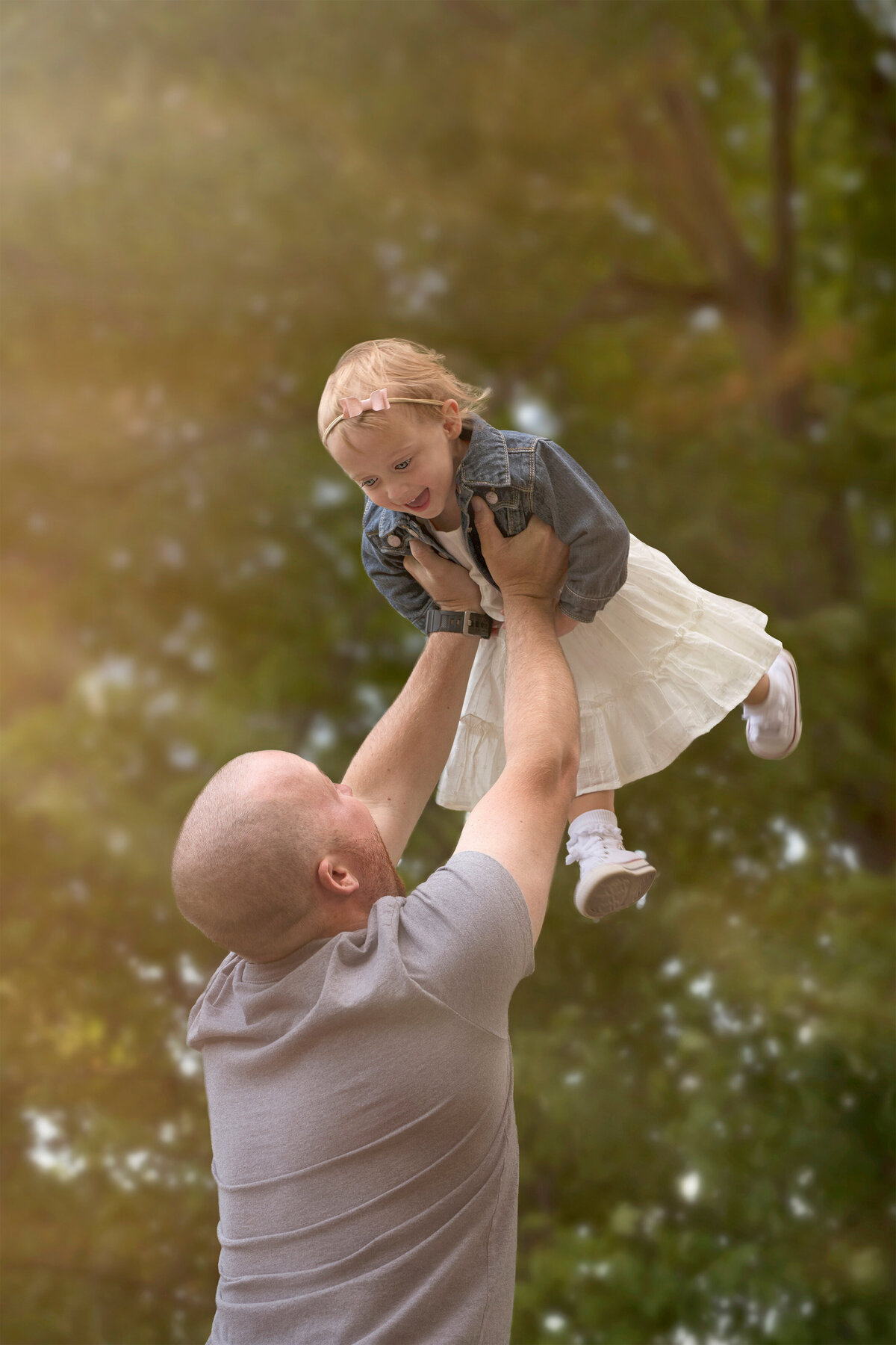 Joyful outdoor family portrait of a father lifting his smiling daughter into the air, captured in Paris, Ontario by Meraki Photographic Creations. Taken at Bronte Provincial Park in Oakville, Ontario.