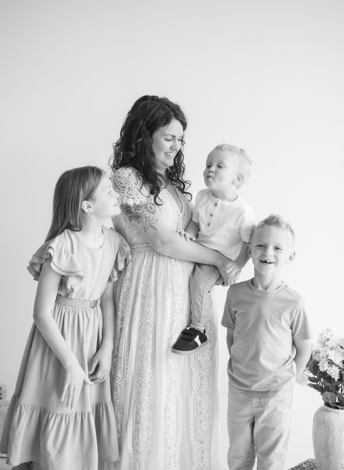 Black and white image of a mother holding her baby while surrounded by her older children during a candid family moment.