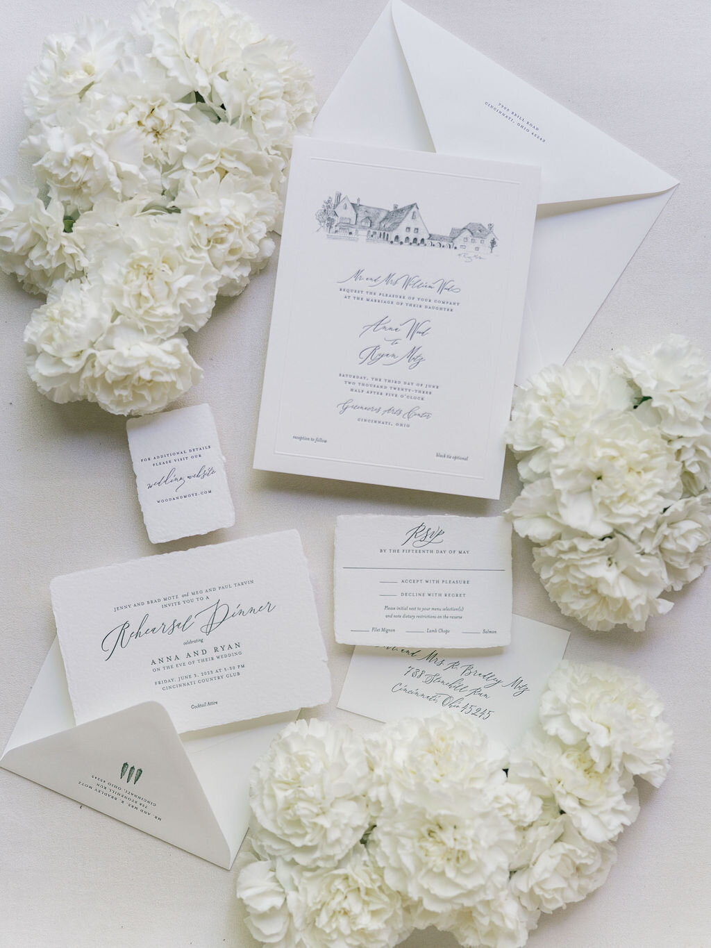 White wedding invitation suite displayed with white flowers.