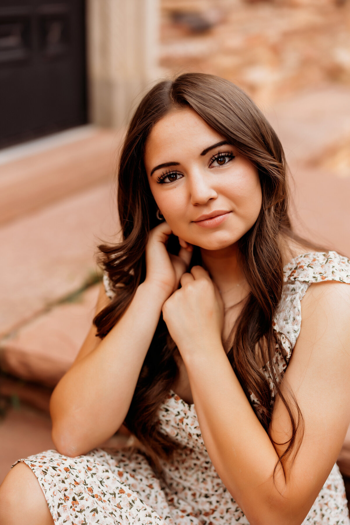 High school senior girl poses on steps while holding her hands to her cheeks during senior photos