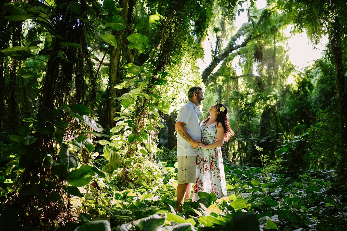 A man and a woman embrace looking at each other in a green luscious forest in Maui.