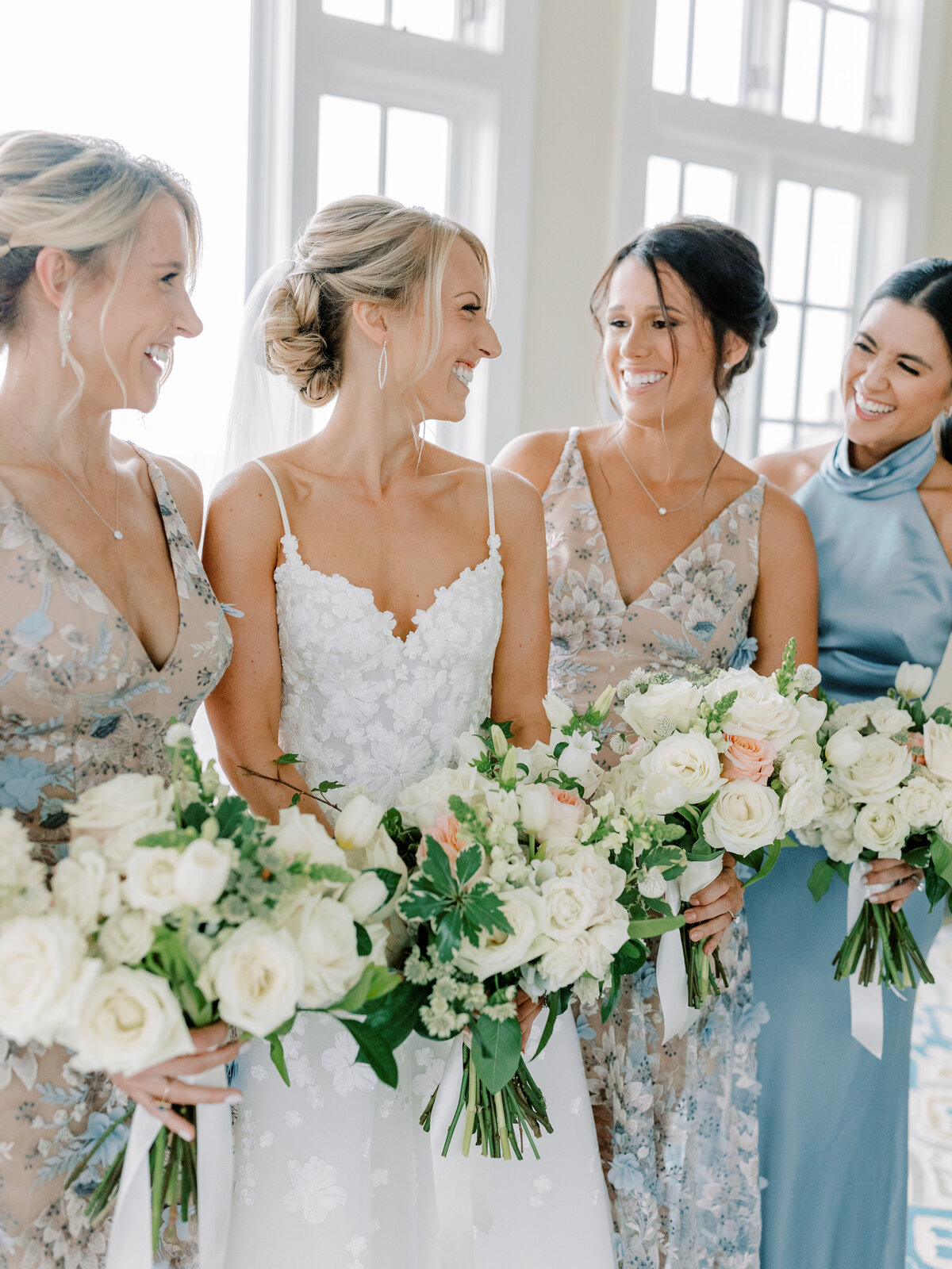 Bride smiling at her bridesmaids in floral dresses holding big white and green bouquets