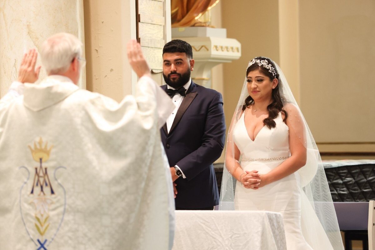 Priest offers blessing to couple as they stand before altar