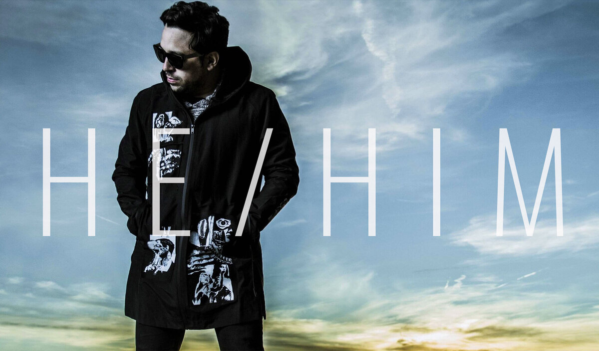 Male musician photo Dagg3rs wearing black coat with white writing standing against desert sunset background