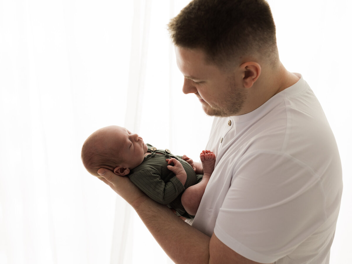 dad in white tshirt holding newborn baby boy in green onesie cleveland newborn photographer
