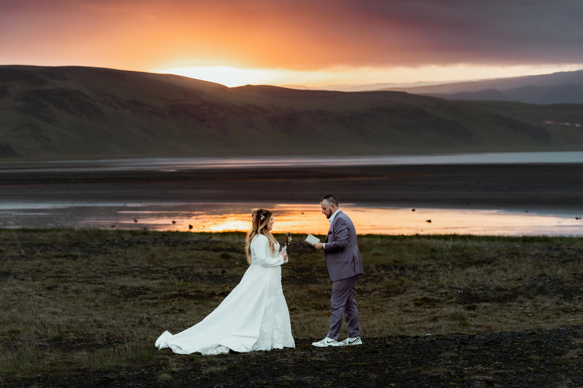 A couple exchanges a tender kiss under the soft glow of sunset on an Icelandic fjord, the calm waters mirroring their peaceful and loving ceremony.