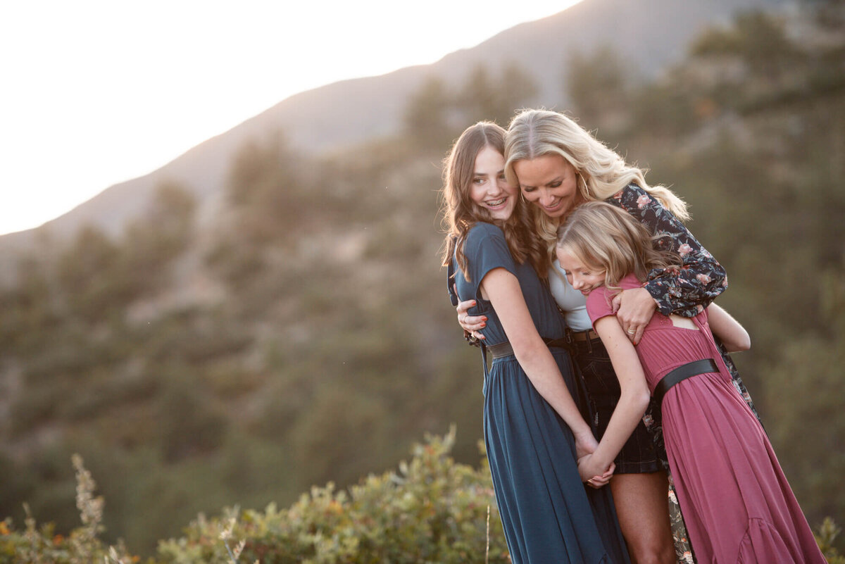 Two Sisters hold hands while hugging their mother on a trail at sunset