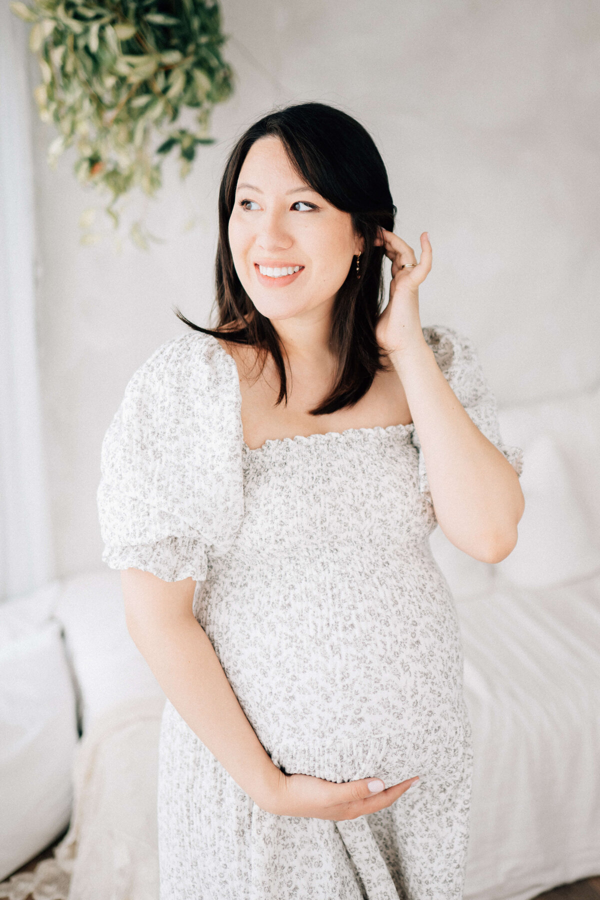 a pregnant woman tucking her hair behind her ear while looking towards a window