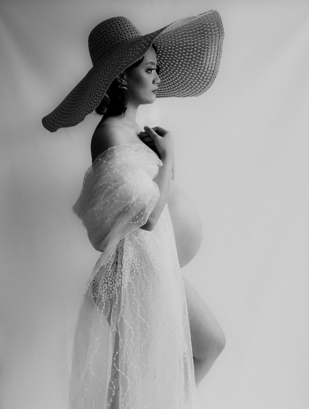  A full-body portrait of a pregnant woman . She is wearing a long, elegant white dress and is looking down at her baby bump with a serene expression. Her hands are resting on her belly, emphasizing her pregnancy.