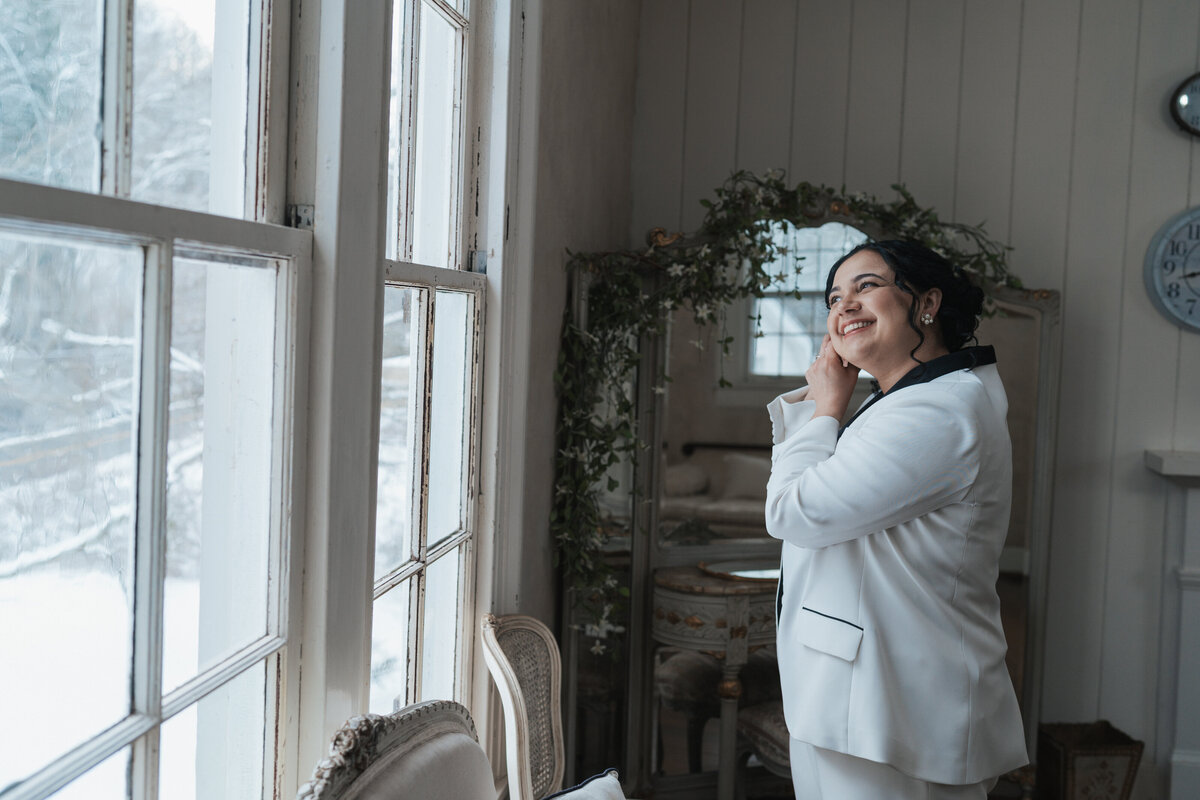 Bride puts on her earrings while looking out the window 