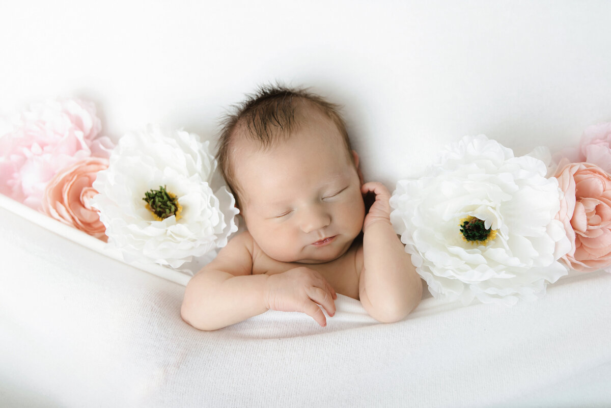 baby girl under white blanket with flowers on both sides of her face