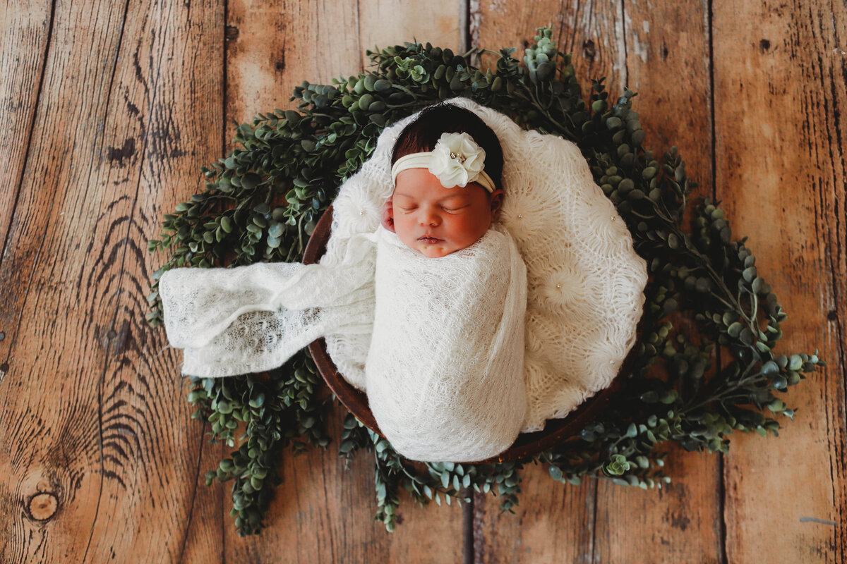 newborn girl in white wrap with white flower