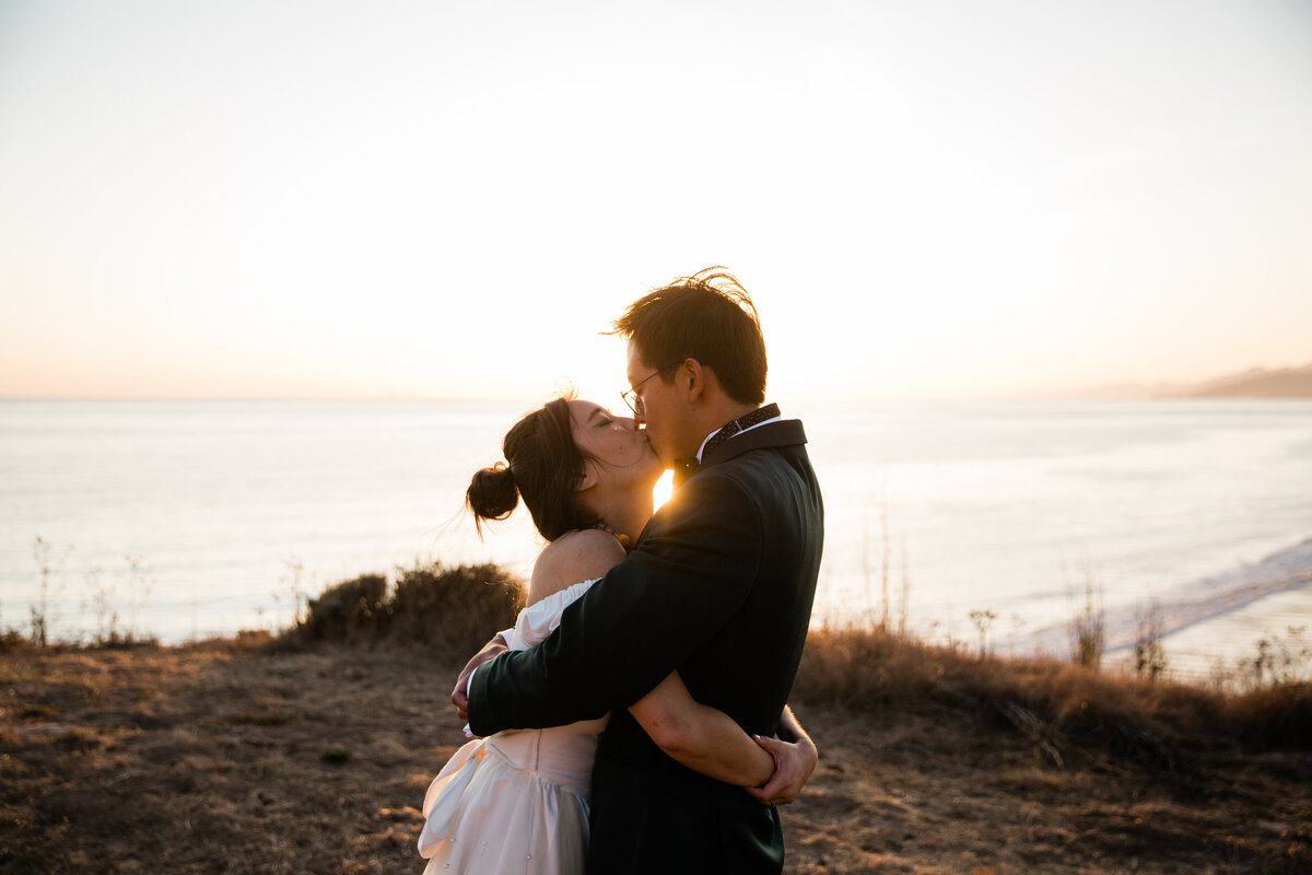 A portrait of the loving bride and groom embraced and having a kiss during sunset at Dos Pueblos Orchid Farm in Santa Barbara along the California coast.