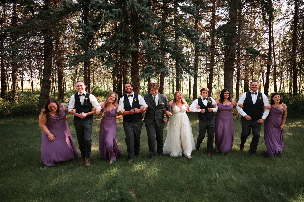 Wedding party all standing together arms linked walking towards the photographer, singing a song, laughing and joking for a candid style wedding portrait