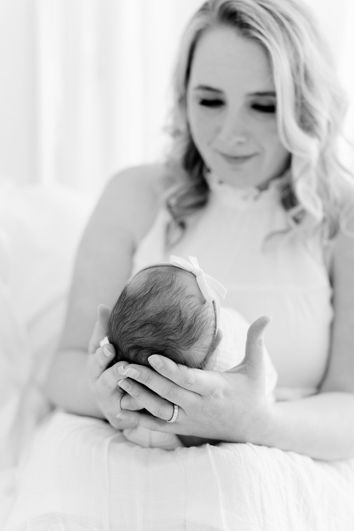 A black & white DC newborn photography image of a mother holding her newborn daughter on a bed