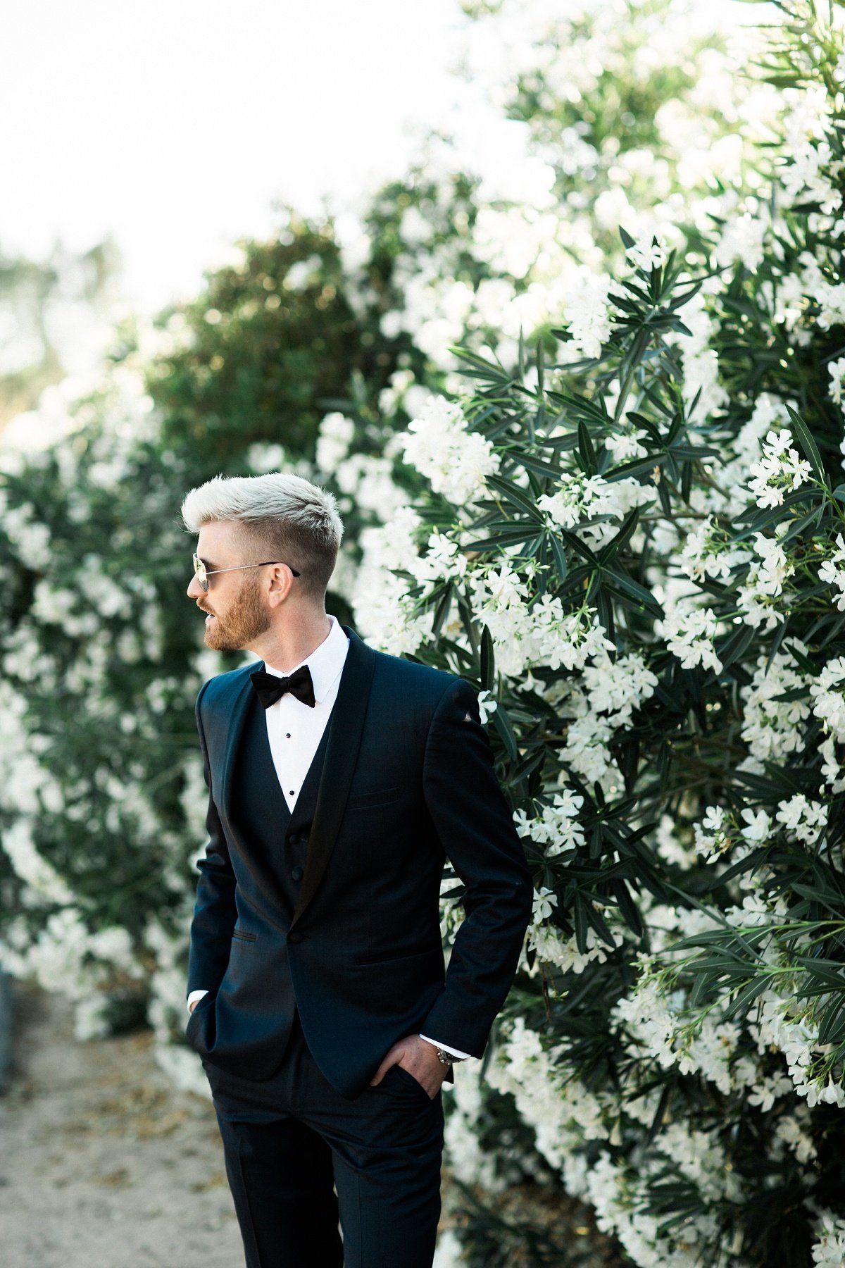 Groom poses next to wall of flowers prior to the wedding ceremony