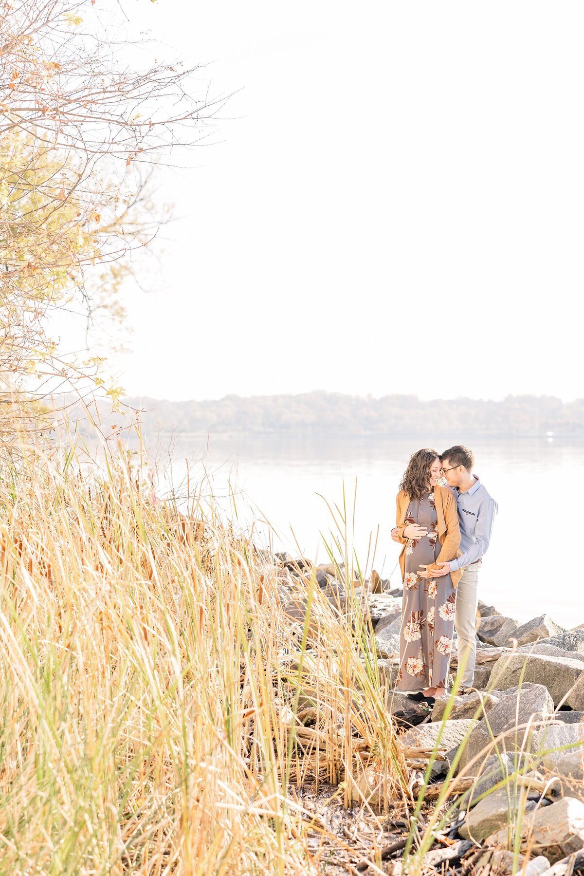 Expectant parents standing forehead to forehead near a river for Ohio family photographer