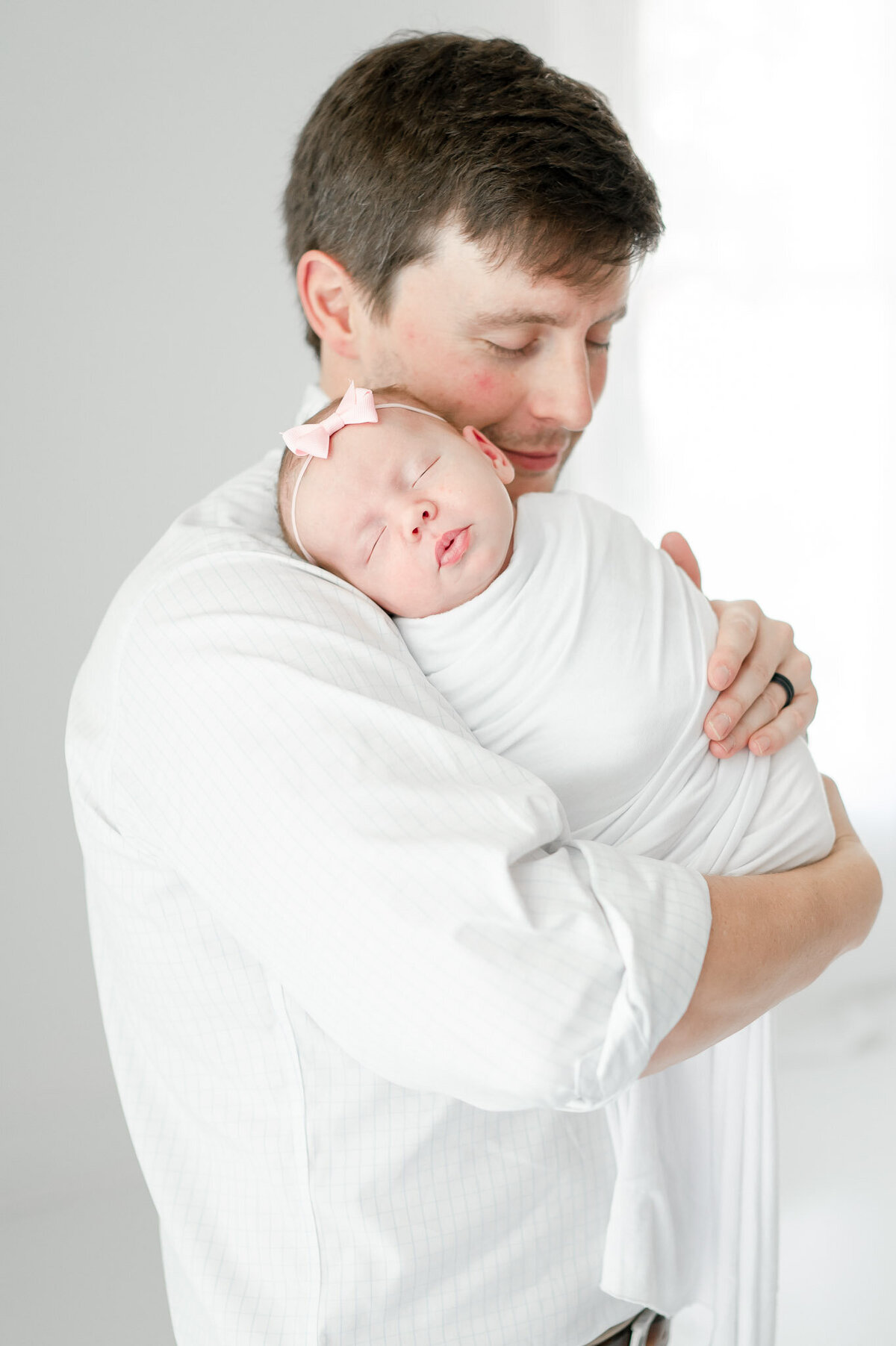 A father holds his newborn daughter in all white Nashville studio
