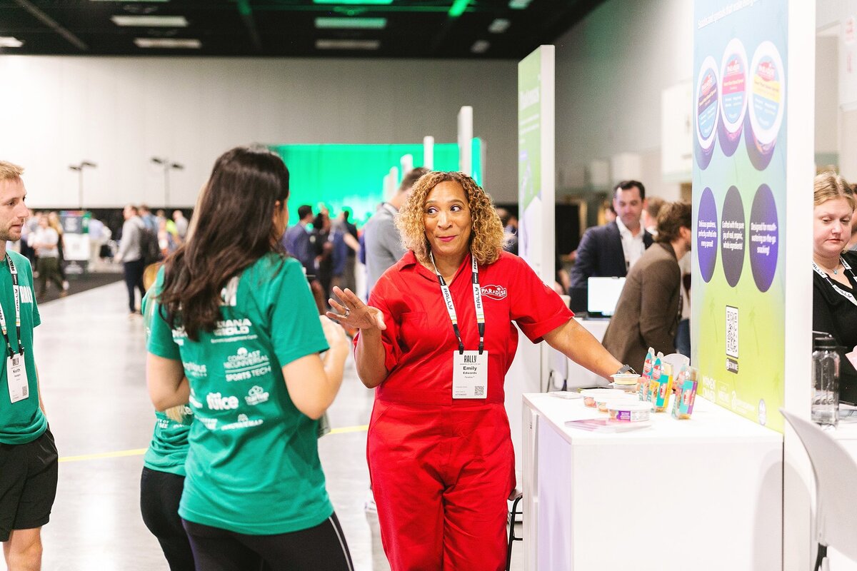 an-exhibitor-in-a-red-jumpsuit-interacts-with-attendees-at-the-rally-conference-in-indianapolis-showcasing-her-brand-at-an-industry-event