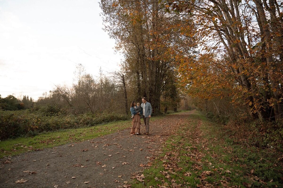 male and female walking on nature path holding newborn son in fall
