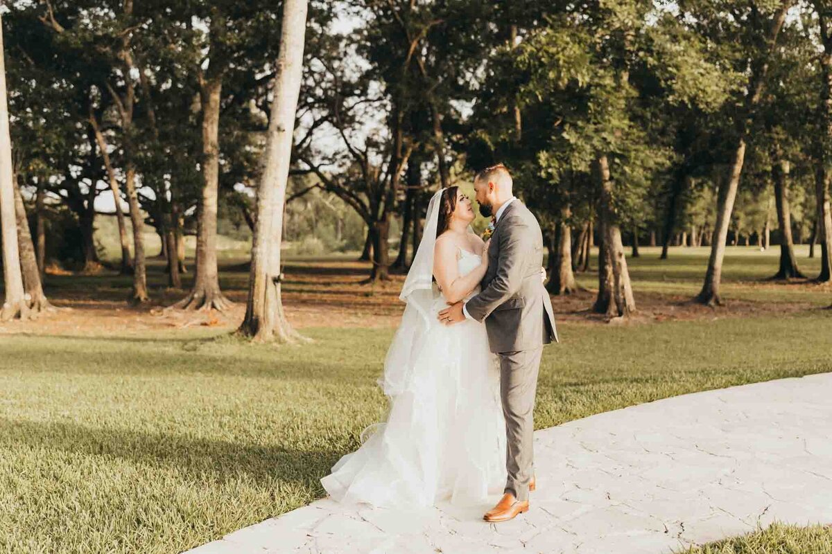 Bride and groom pulled in close, kissing underneath trees.