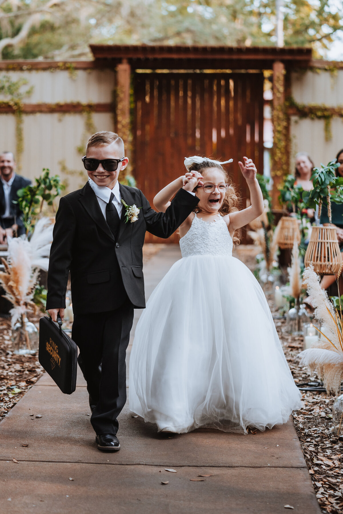 flower girl and ring bearer walking down aisle together smiling and laughing