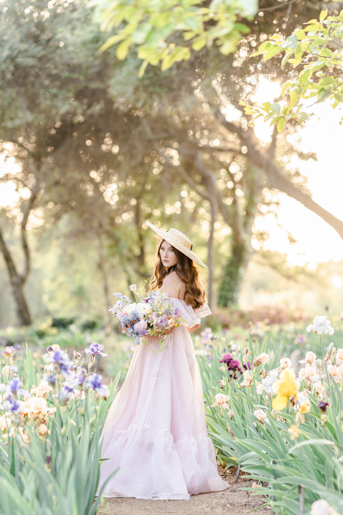 A woman wearing a lavender gown holding a bouquet of irises and standing in an iris garden photographed by Bay area photographer, Light Livin Photography.