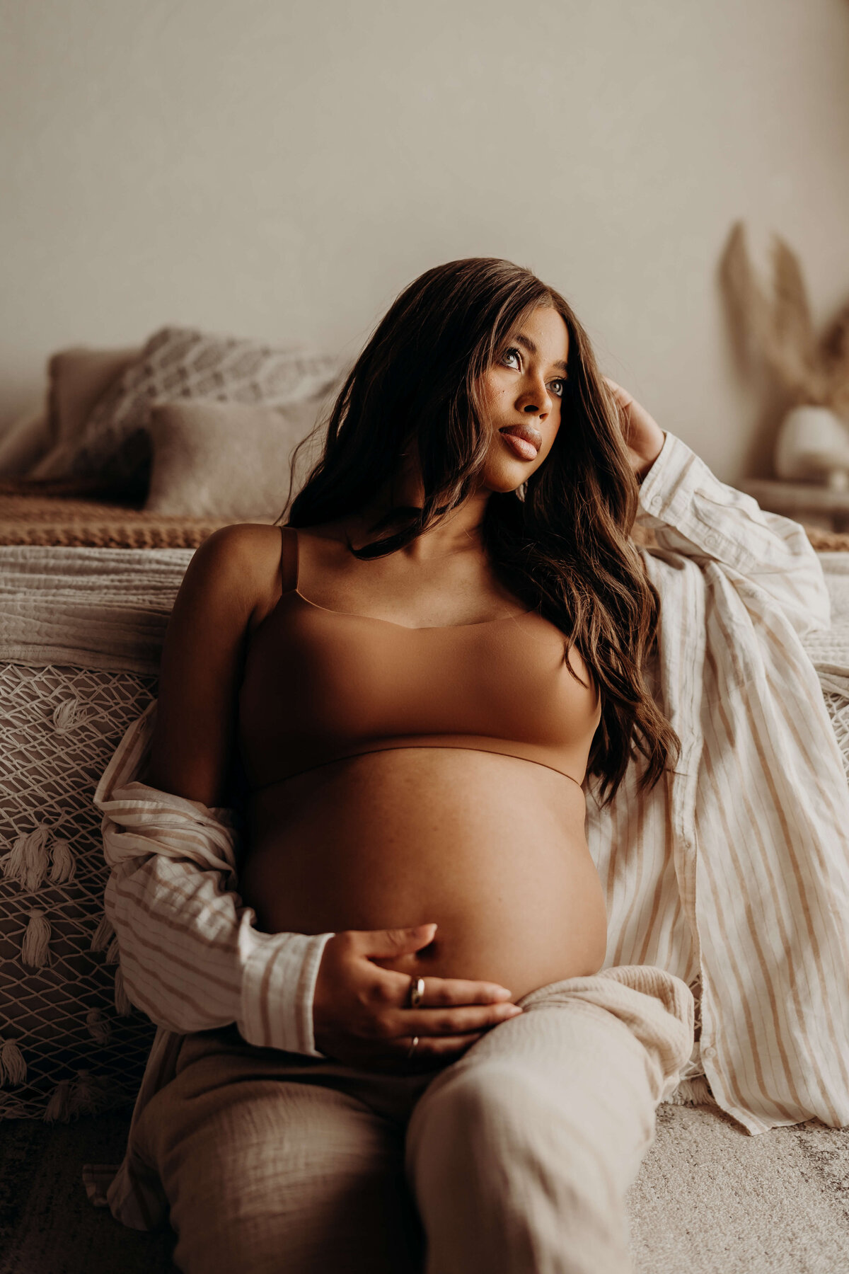 maternity portrait of woman on floor leaning against bed in linen pajamas