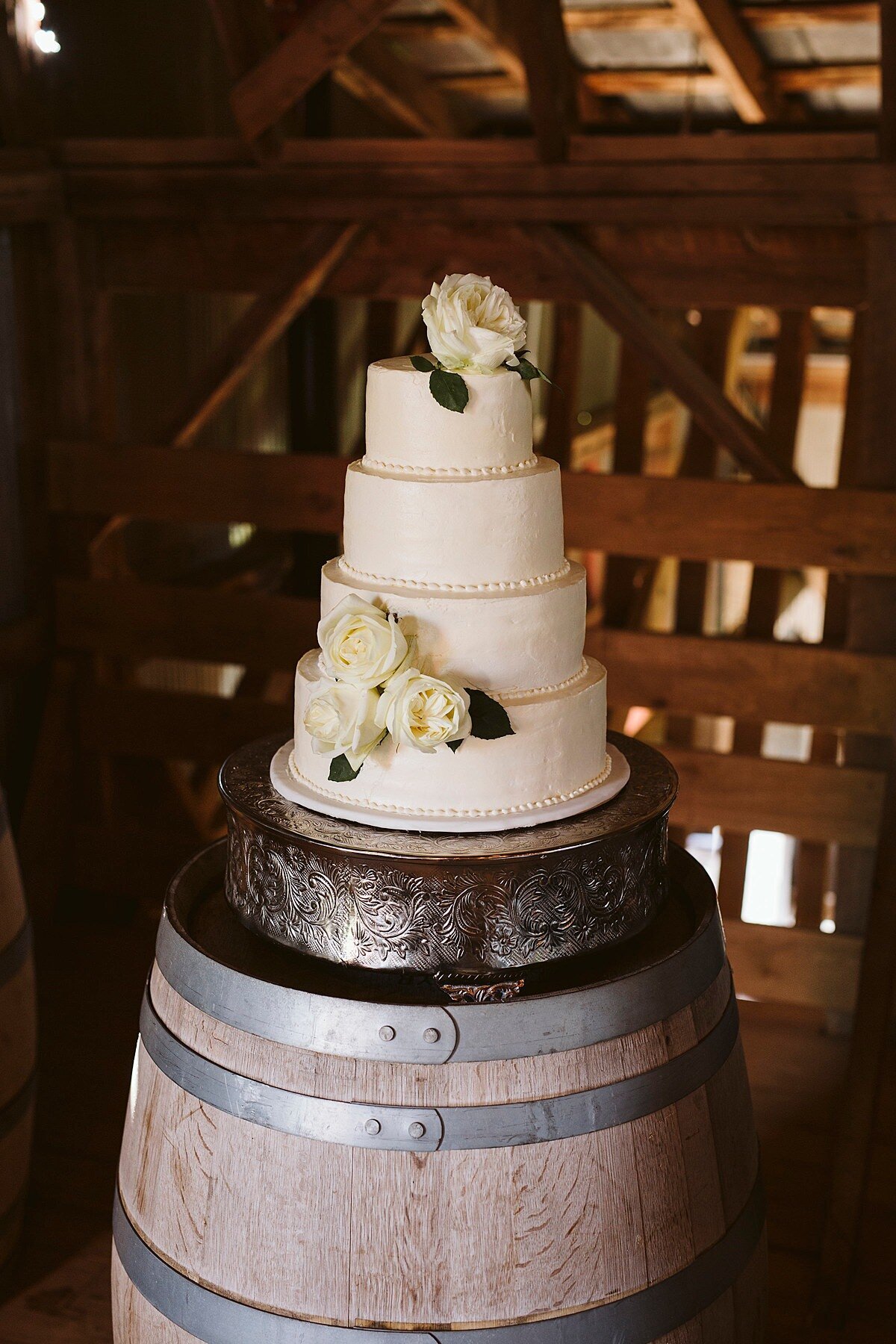 4 tier white wedding cake on a silver cake stand sitting on a large wine barrel at Arrington Vineyards.