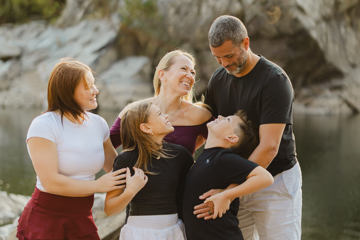 A family of five laughs while in front of a rocky outcliff.