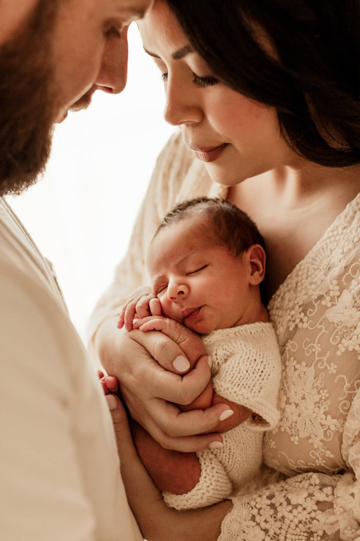 Mother an father with their heads touching and peering down at their newborn baby boy sleeping.