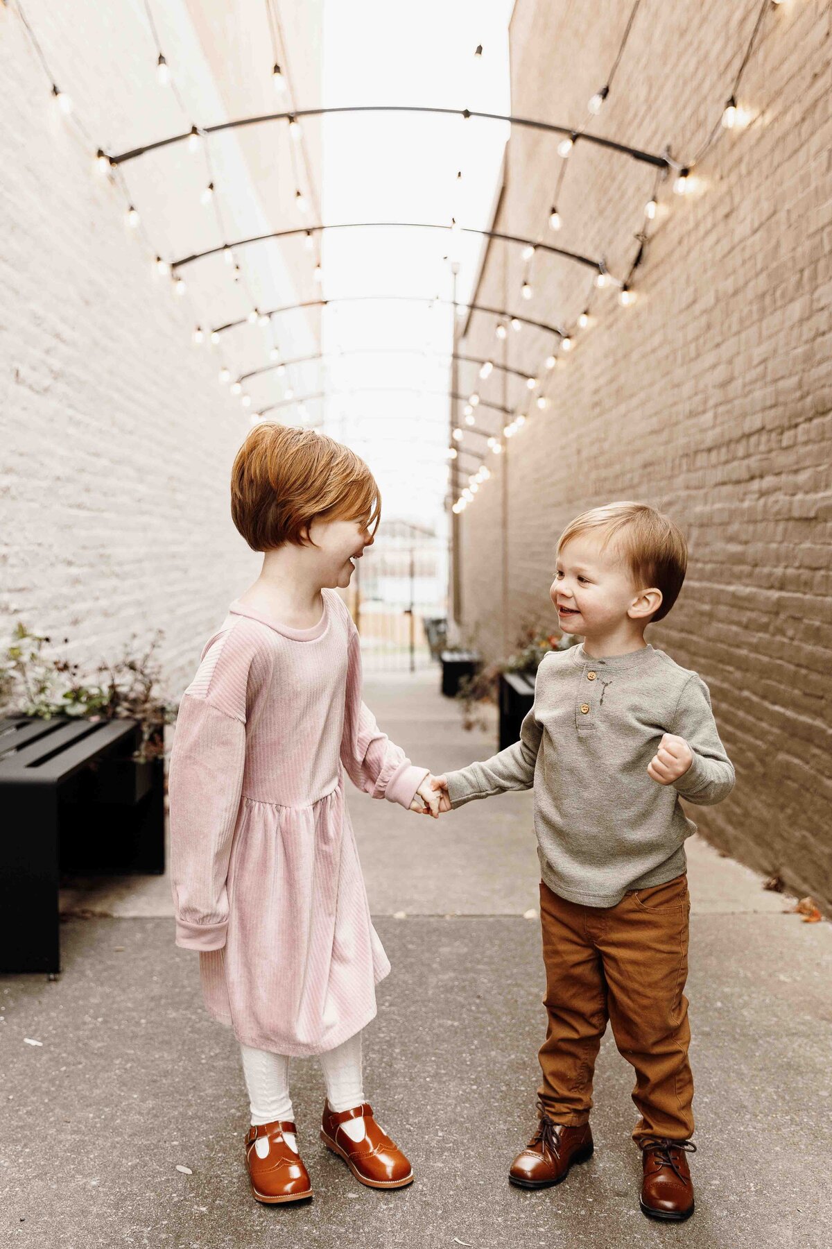 Brother and sister hold hands while laughing and smiling at each other