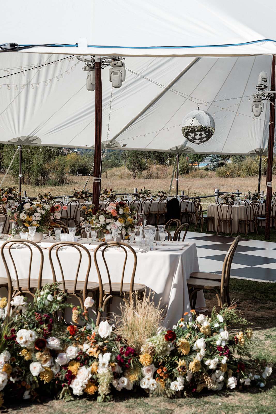 A wedding tent with a hanging disco ball and tables set with tableware and flowers.