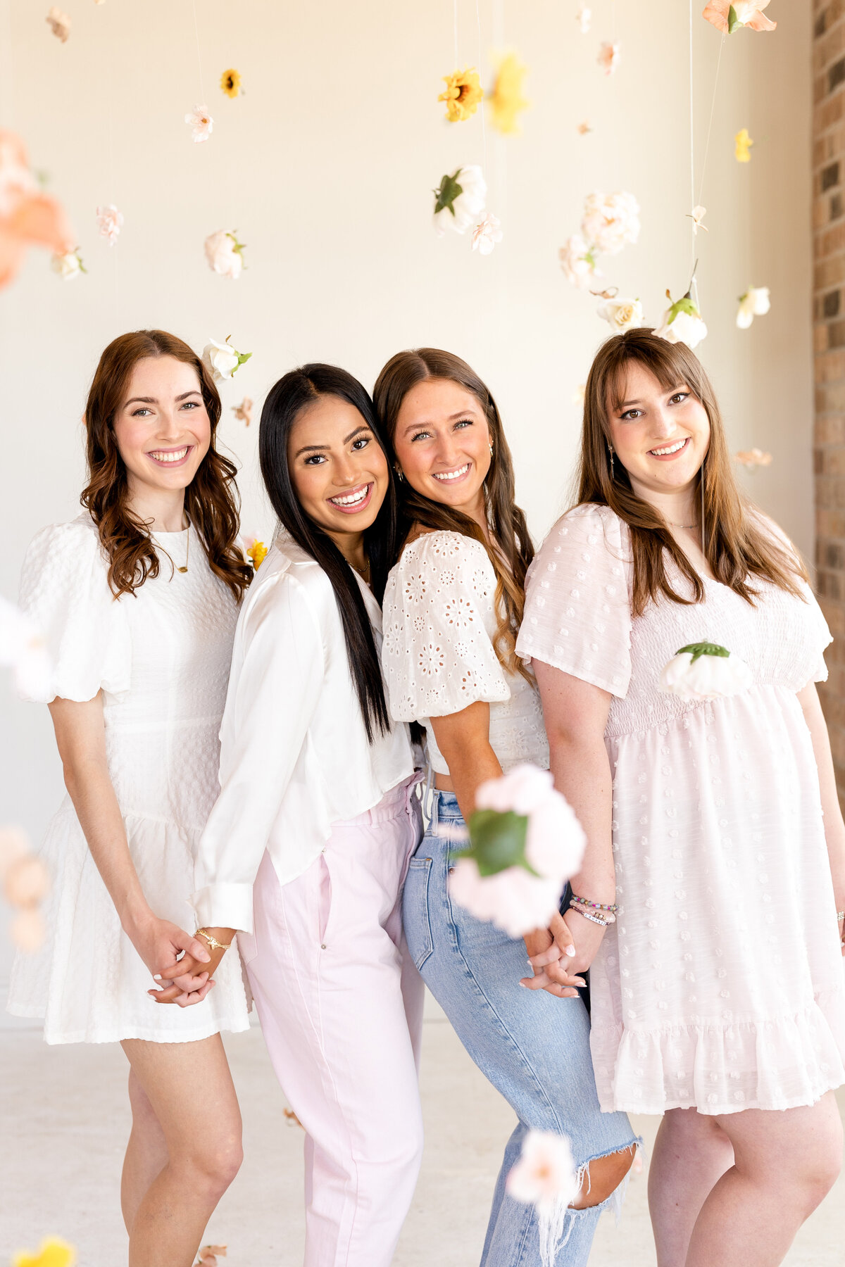 Senior girls holding hands and smiling in the middle of a hanging garden of flowers at Bravely Studio in Downtown Houston