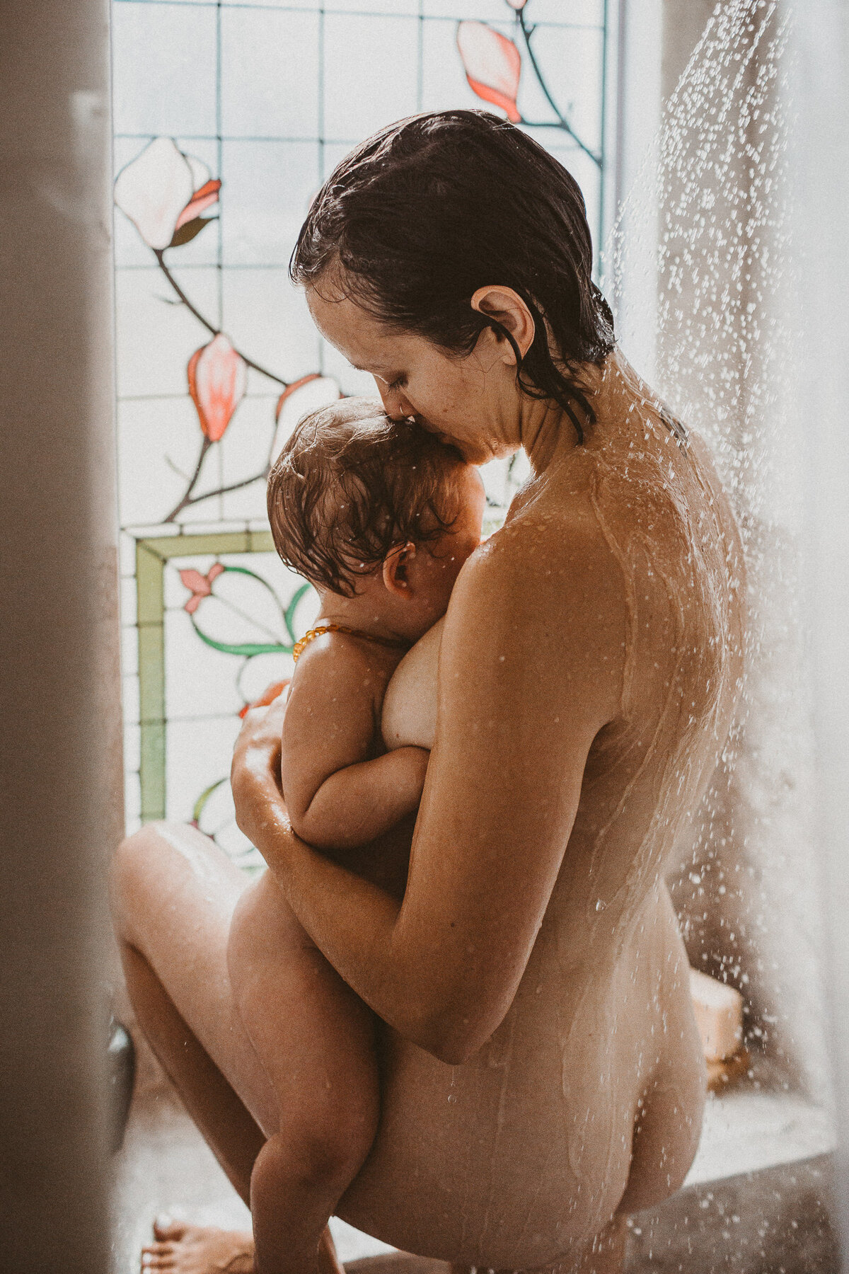 mother nurses baby while in the shower with beautiful stained glass shower