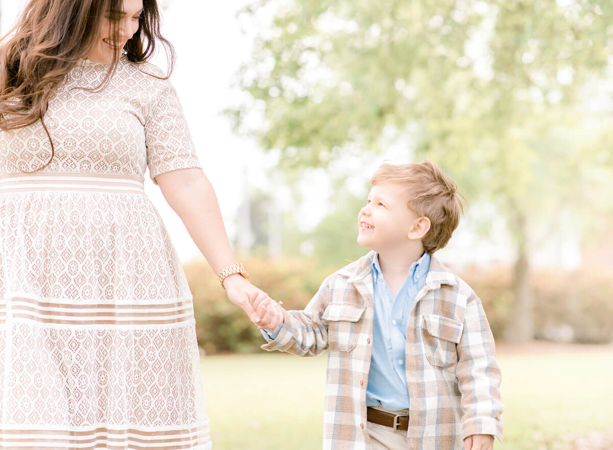 A mother in a lace gown holds hands with her toddler son dressed in tan and blue plaid. Taken in Hammond, LA by Morgan Leigh Photography.