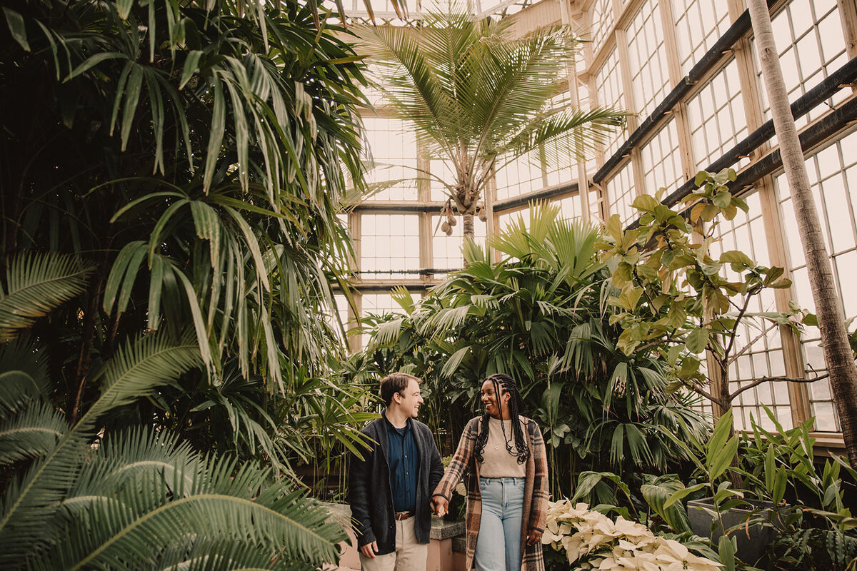 A couple holding hands and walking in a greenhouse 
