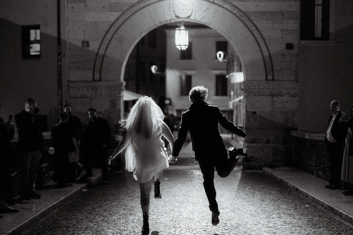 bride and groom skipping away from the camera towards a stone archway