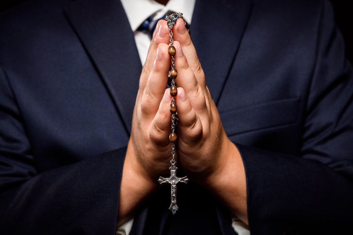 A pair of hands hold a rosary between them in a prayer-like gesture