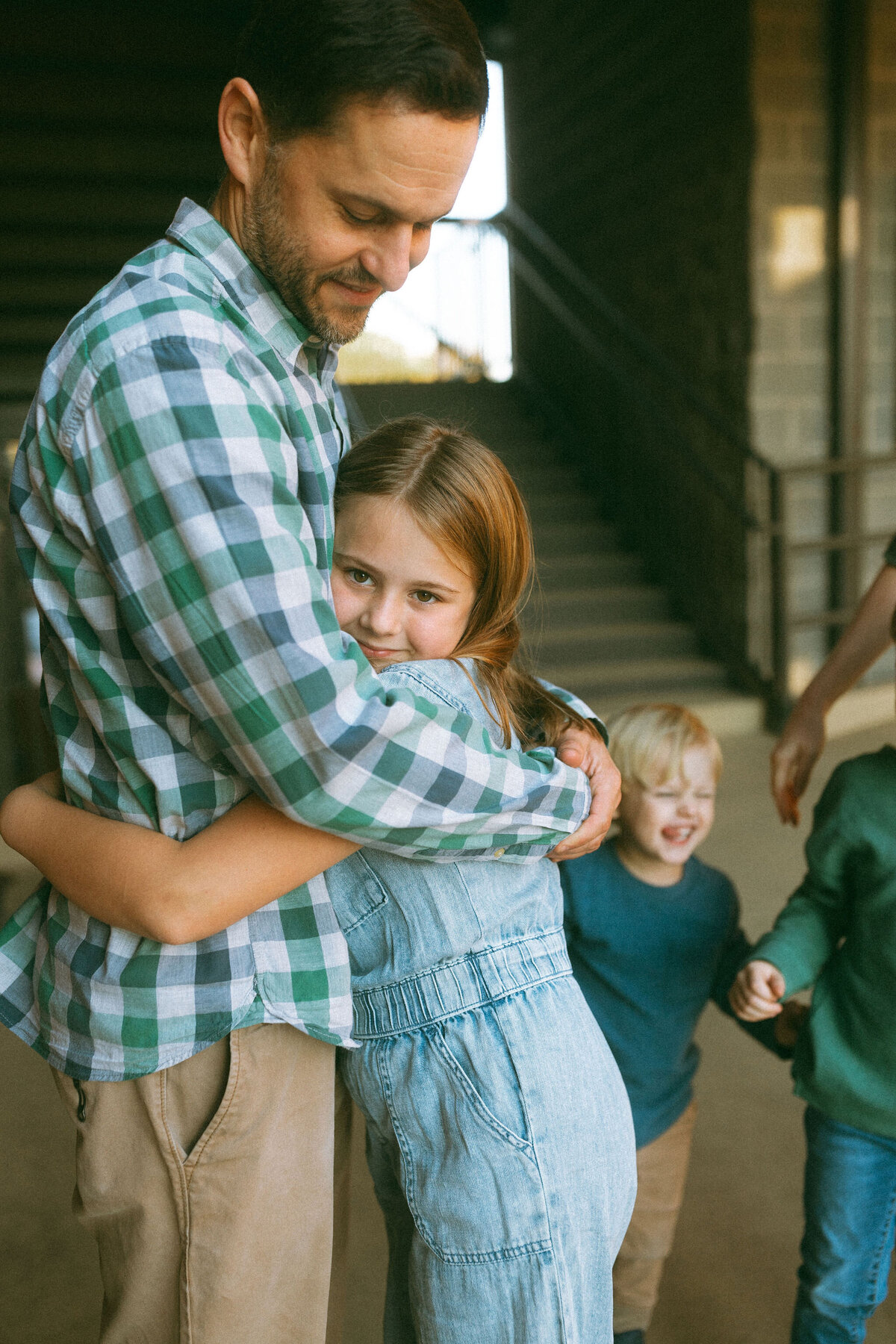 A father hugging his young daughter while their family plays in the background. 