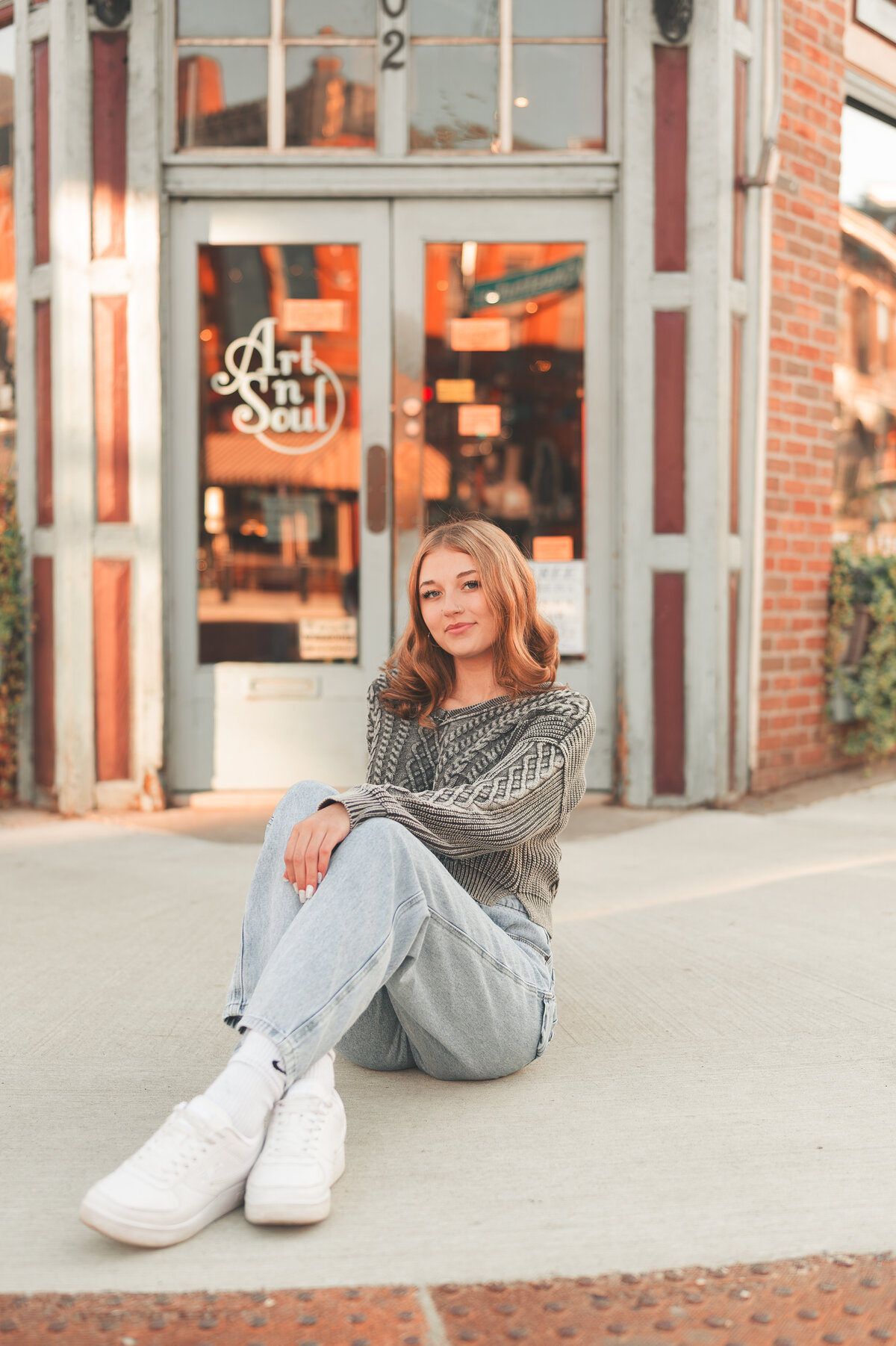 female senior picture sitting on the sidewalk outside of a store doors looking relaxed in Stillwater