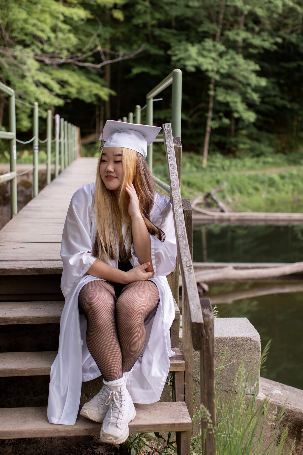 Senior sits on wooden stairs in her cap and gown, looking off into the distance