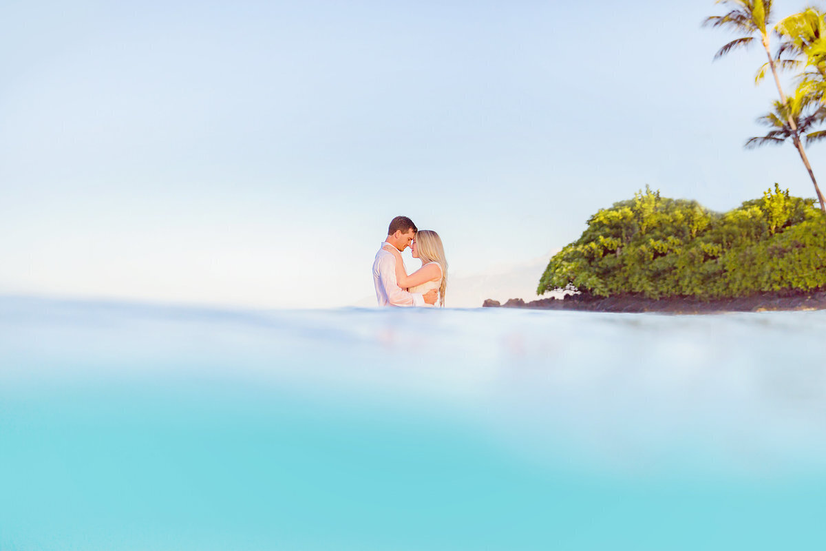 Couple in the ocean hold one another while Love + Water photograph them from the beach in Wailea