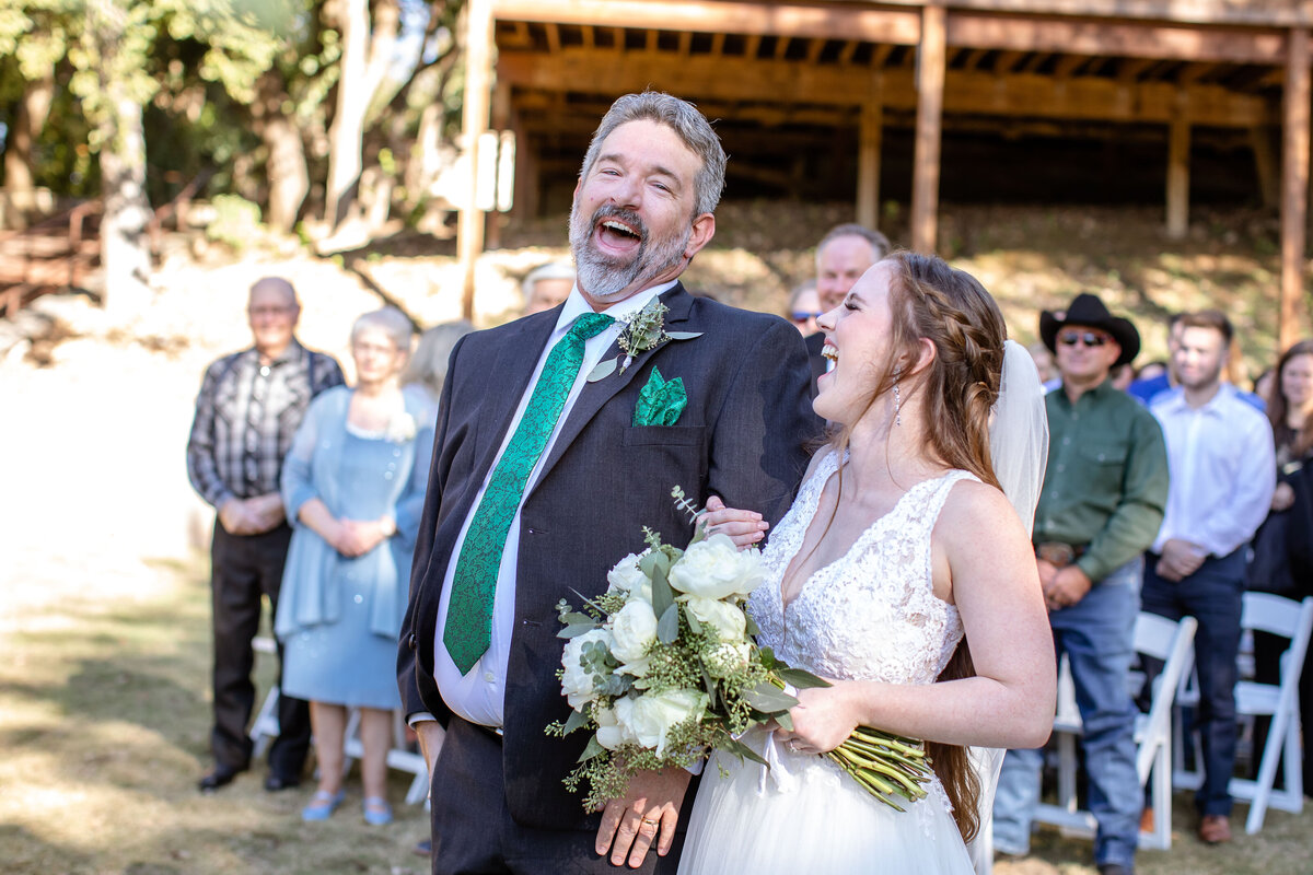 bride and father laugh heartily as they walk down the aisle at Milltown Historic District in New Braunfels Texas