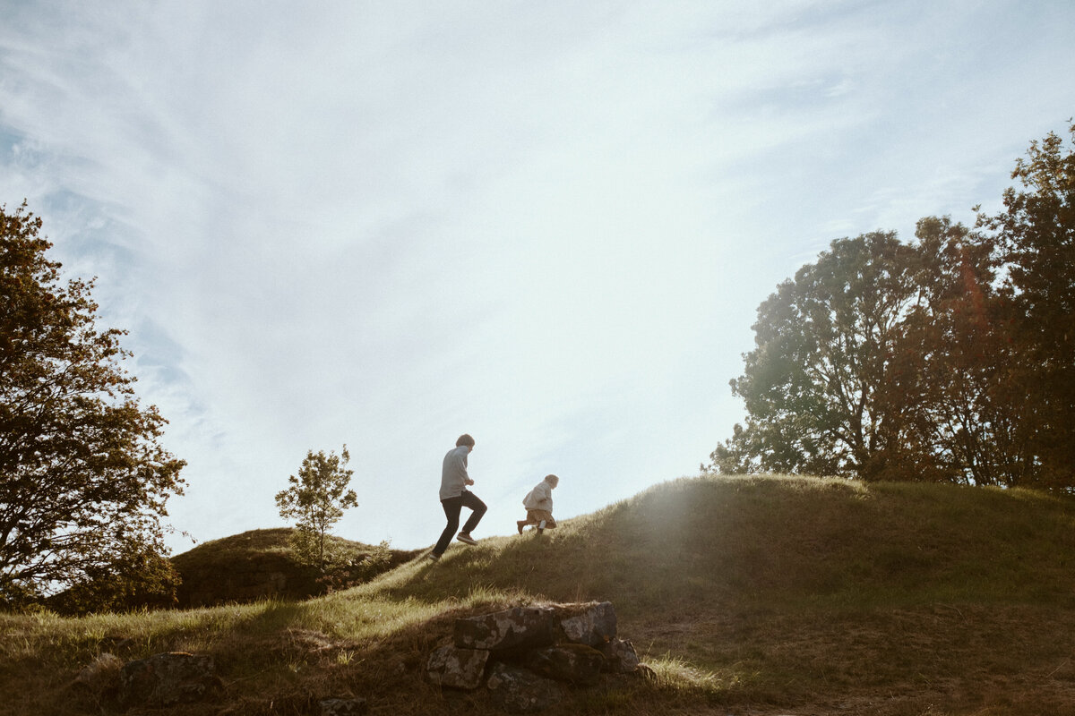 Perhekuva isästä ja hänen 4-vuotiaasta lapsesta juoksemassa mäkeä ylös Suomenlinnassa Helsingissä