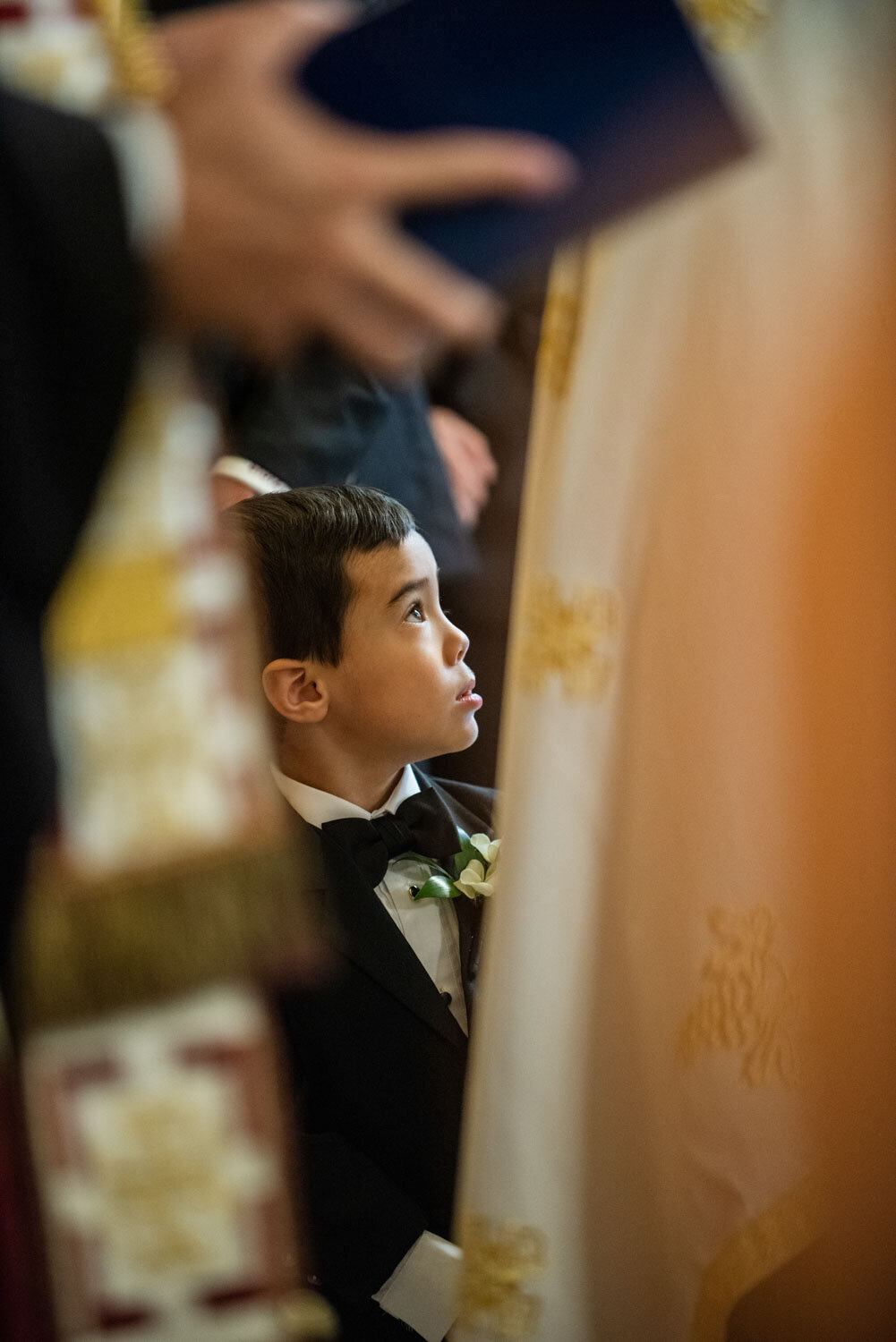 A young boy in a tuxedo looks up at something