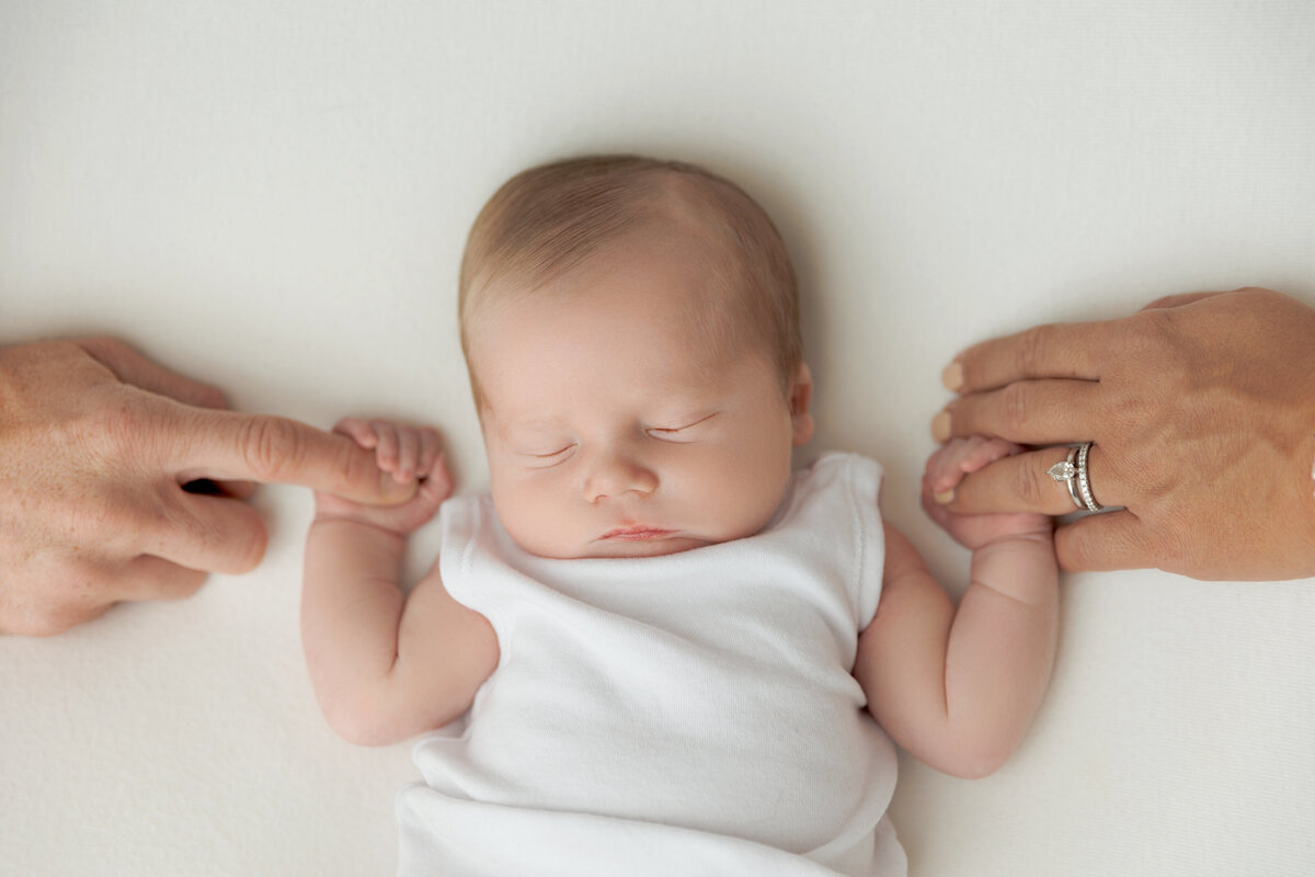 A sleeping newborn baby holds on to mom and dad's fingers on each side
