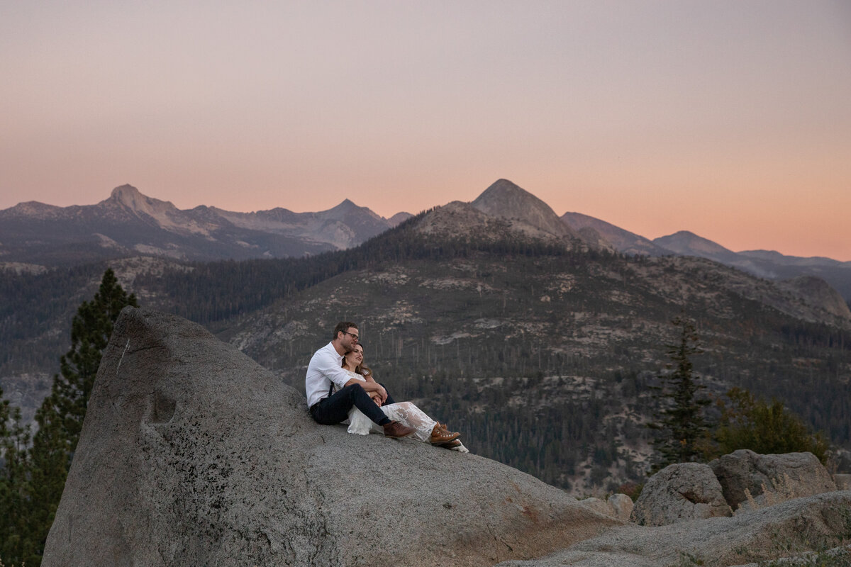 A groom sits on a rock with his bride sitting between his legs and leaning against his chest during their Yosemite elopement.